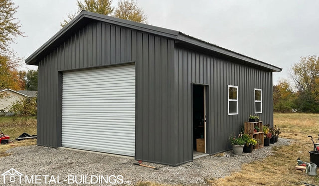 Gray metal garage with a roll-up door and open side door, surrounded by trees and a cloudy sky.