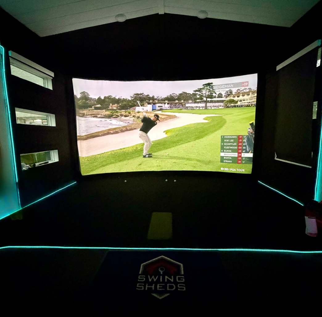 Golf simulator setup with screen displaying a golf course, branded 'Swing Sheds'.
