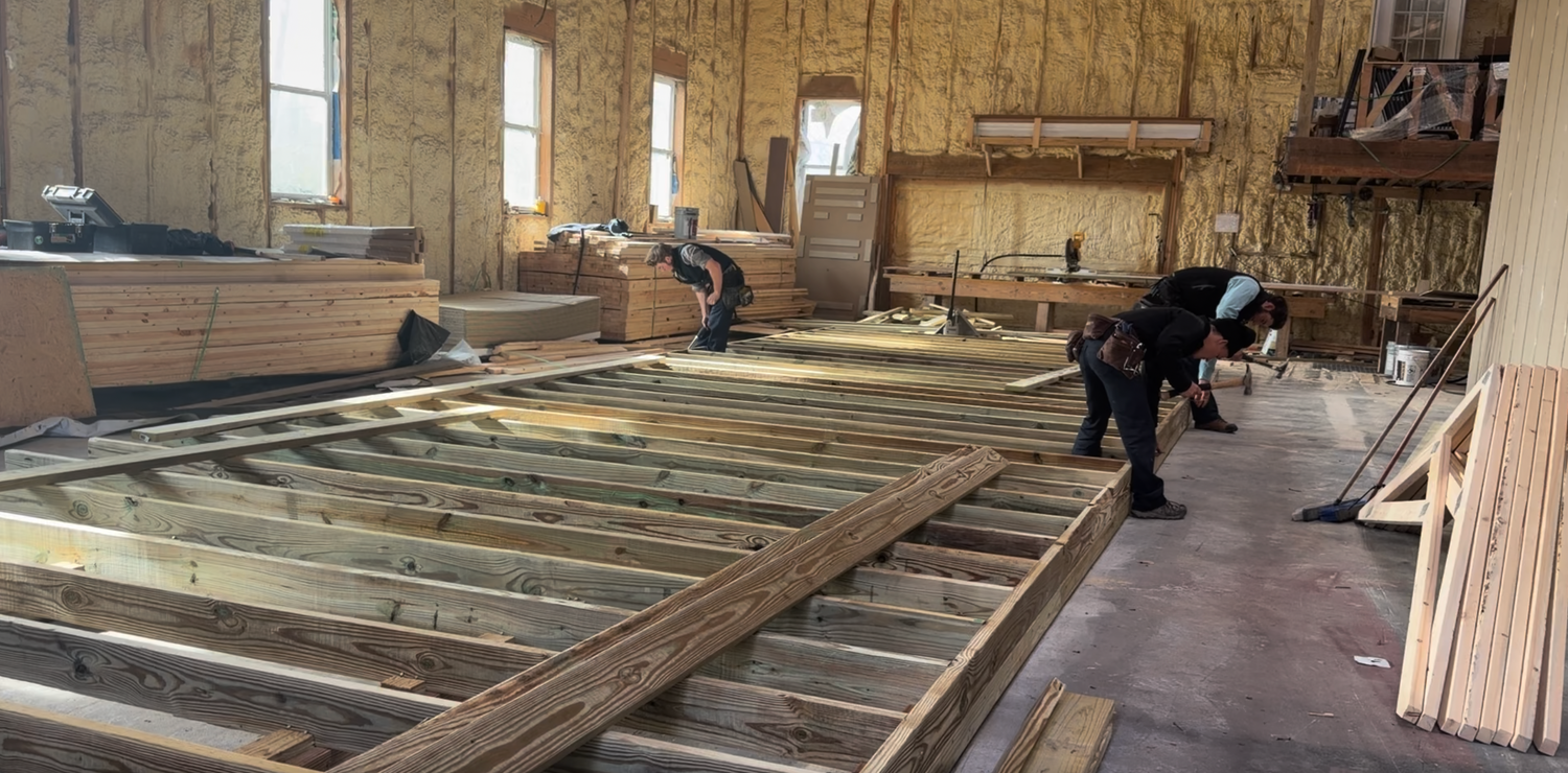 Construction site with wooden floor beams and workers in a partially built room.
