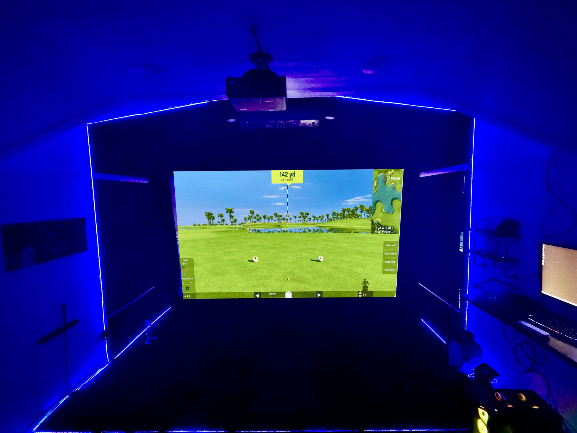 Golf simulator setup with screen displaying a golf course on a dark background